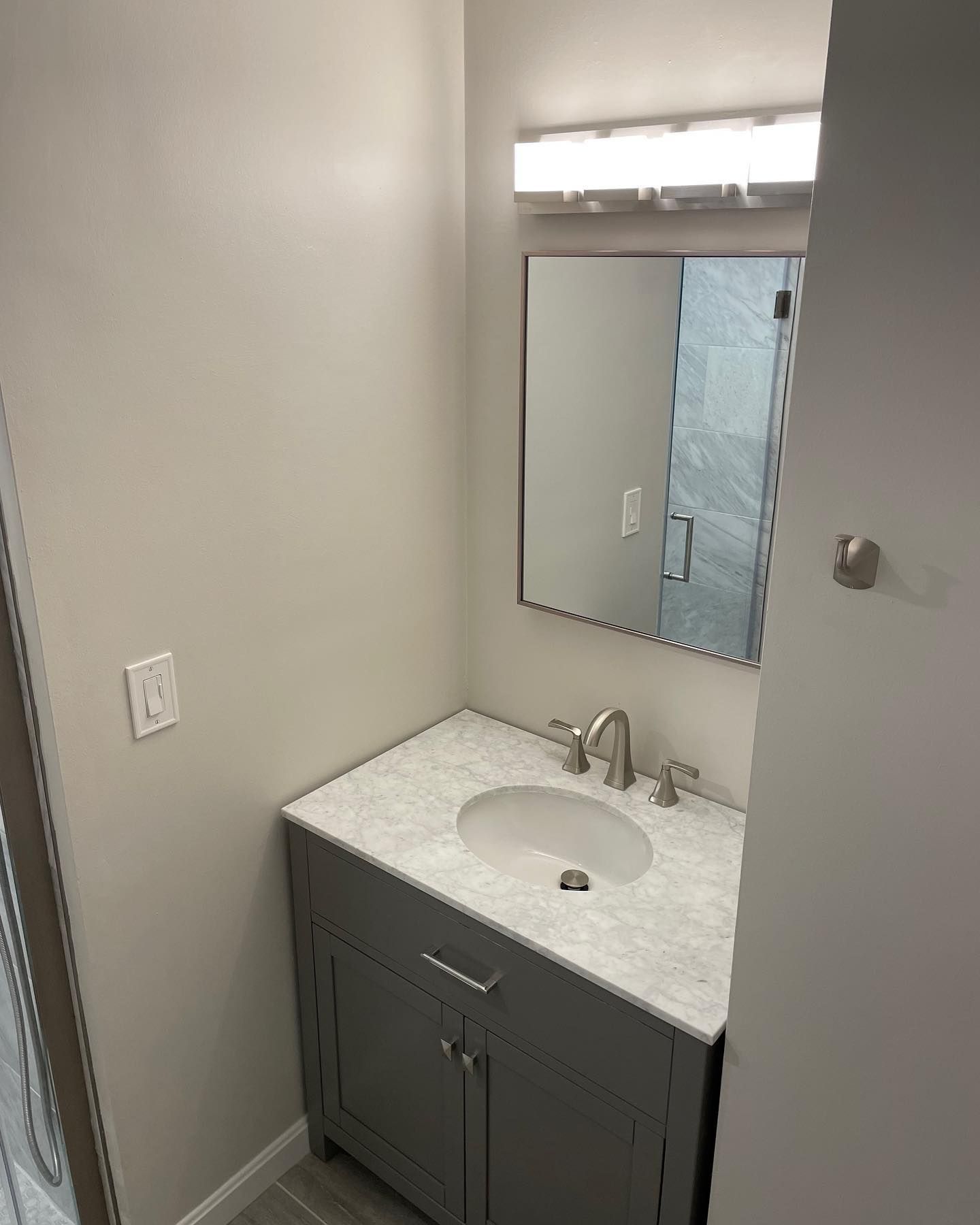 A grey bathroom vanity with a white speckled countertop, silver faucet, rectangular mirror, and light fixture.