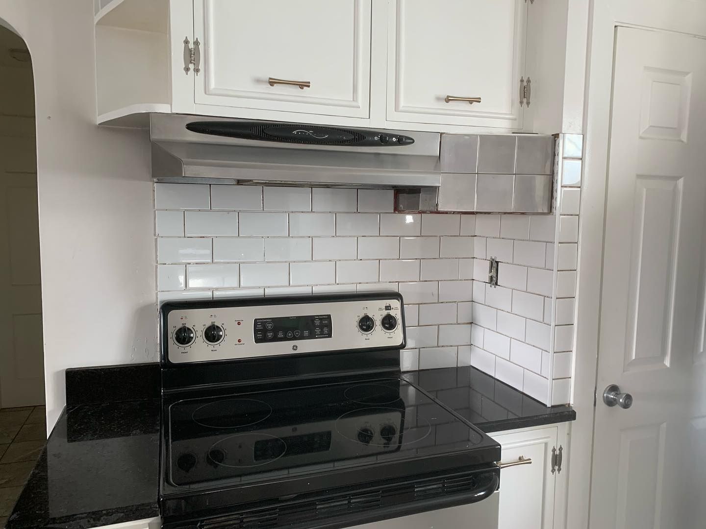 A kitchen stove with a black surface, stainless steel hood, and white subway tile backsplash under white cabinets.