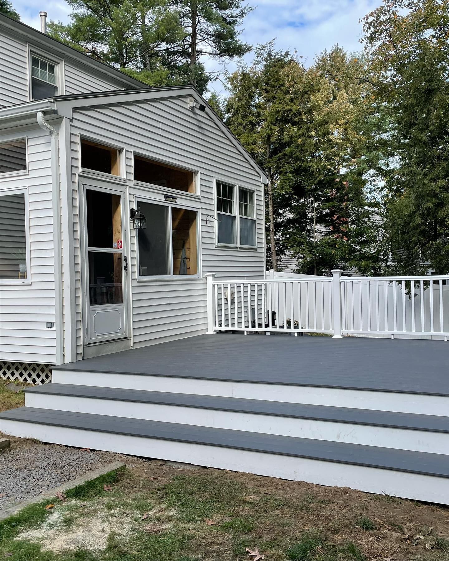 A white house with a gray deck featuring three steps and a white railing in a grassy backyard.