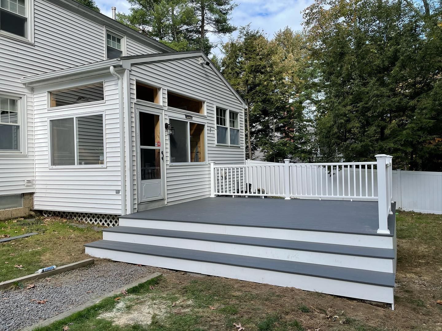 A white vinyl-sided house extension features a newly constructed gray deck with white railings and three wide steps.