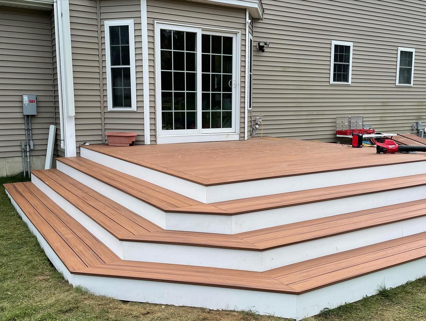 A three-tiered deck with brown composite boards and white risers attached to the back of a house with tan siding.