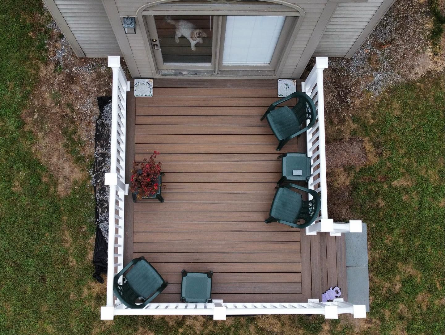 An aerial view of a wooden backyard deck with outdoor furniture and a sliding glass door showing a dog inside.