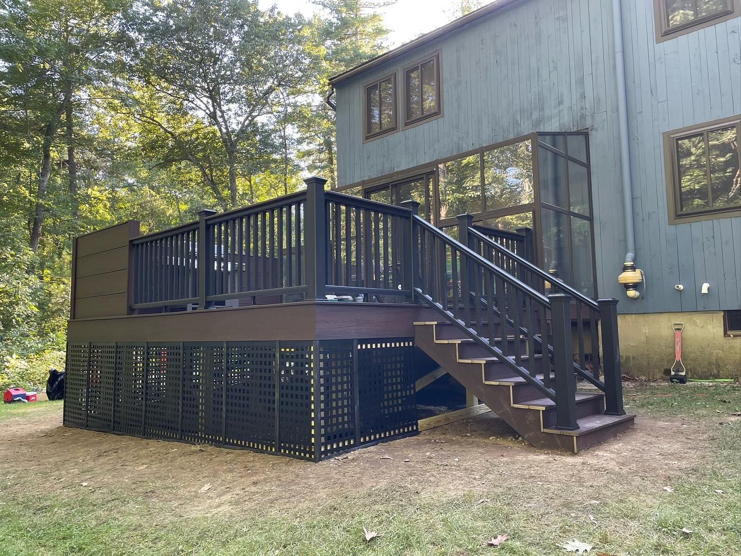 A dark-colored, elevated deck with a matching staircase and lattice skirting, attached to the back of a grey house.