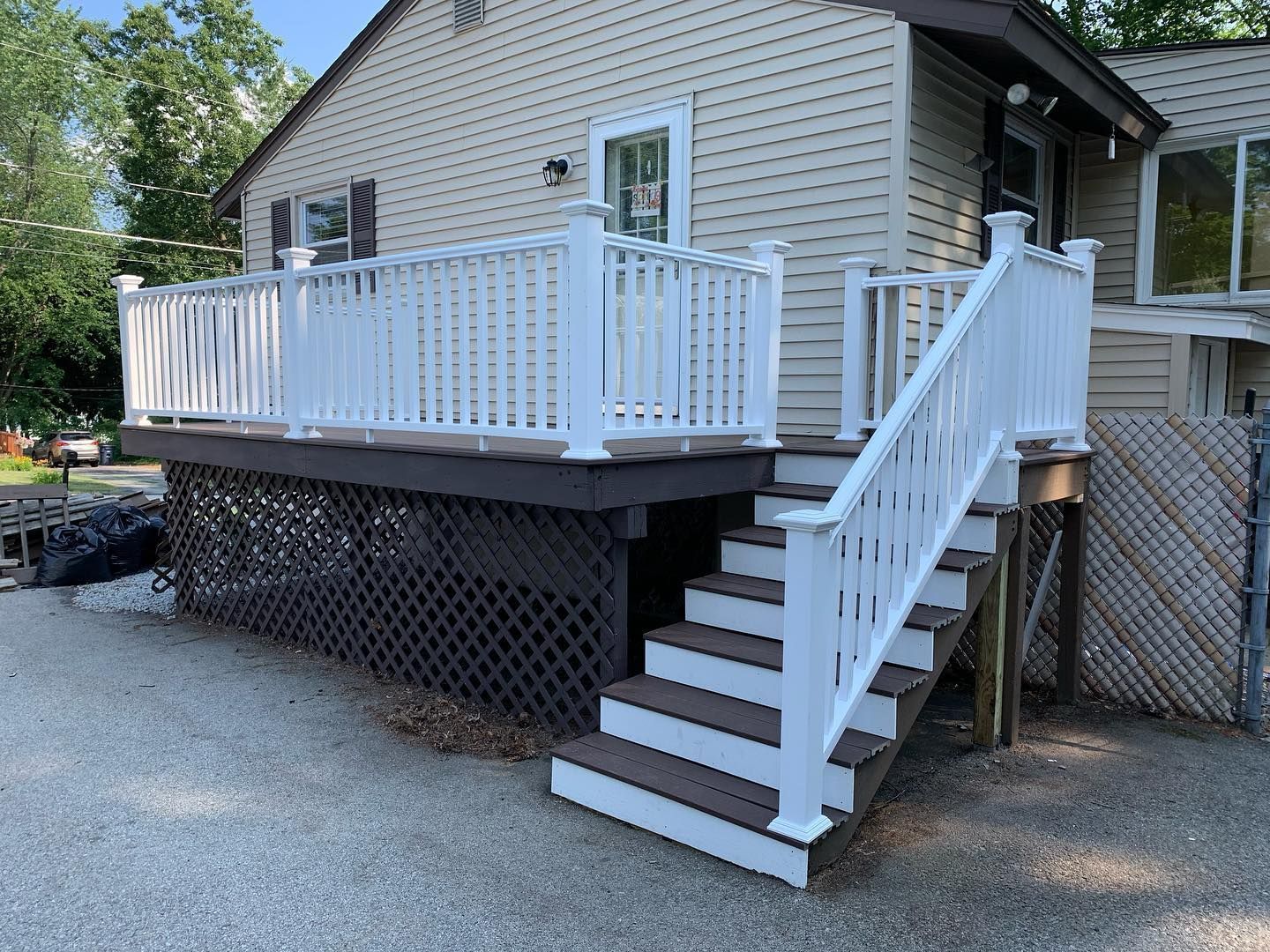 An elevated wooden deck with white railings and stairs leads to the side entrance of a house with beige siding.