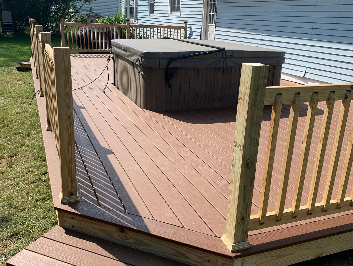 A brown composite deck featuring a covered hot tub, surrounded by wooden railings, next to a house exterior.