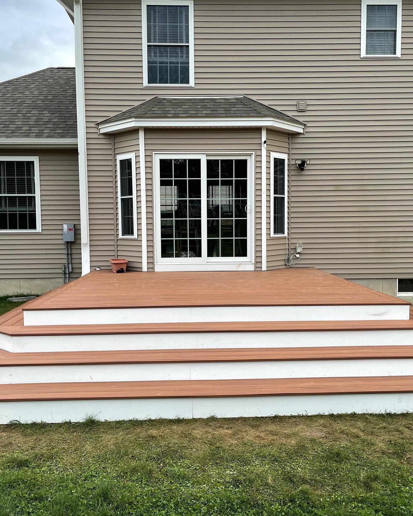 A newly built, tiered wooden deck with white risers attached to the rear exterior of a beige, vinyl-sided suburban house.
