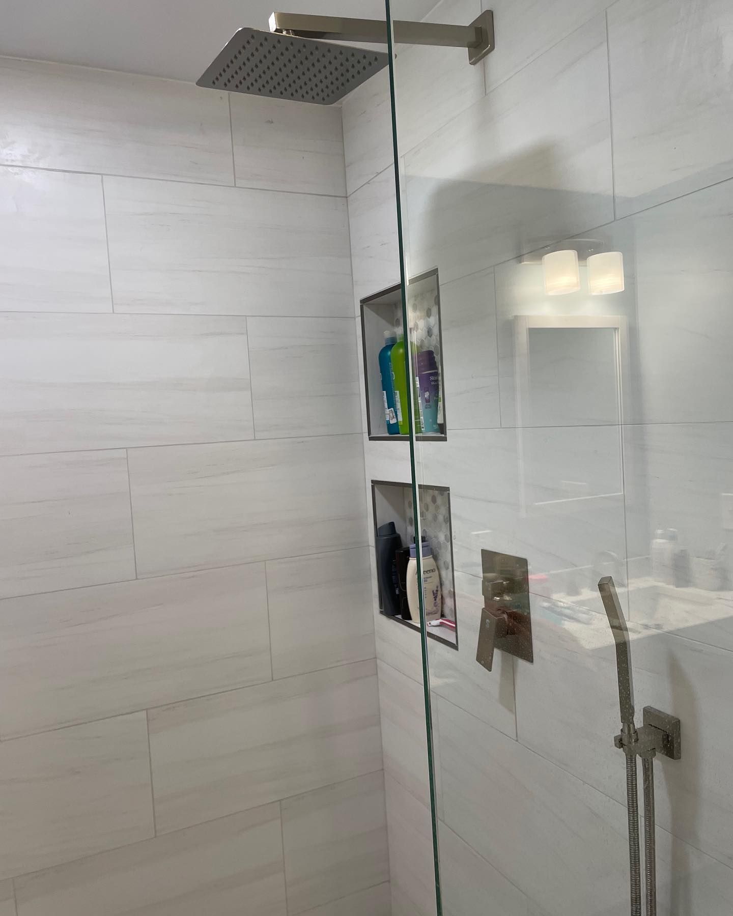 Modern walk-in shower with white tiled walls, two recessed storage niches, a rain showerhead, and a handheld fixture.