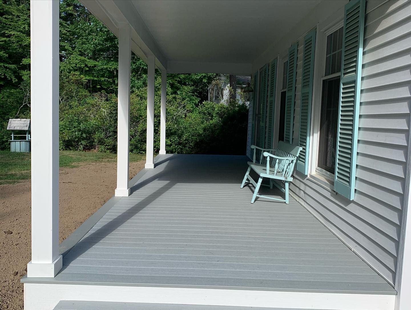 A white house with a gray porch, tall white columns, light blue shutters, and a small matching blue bench.