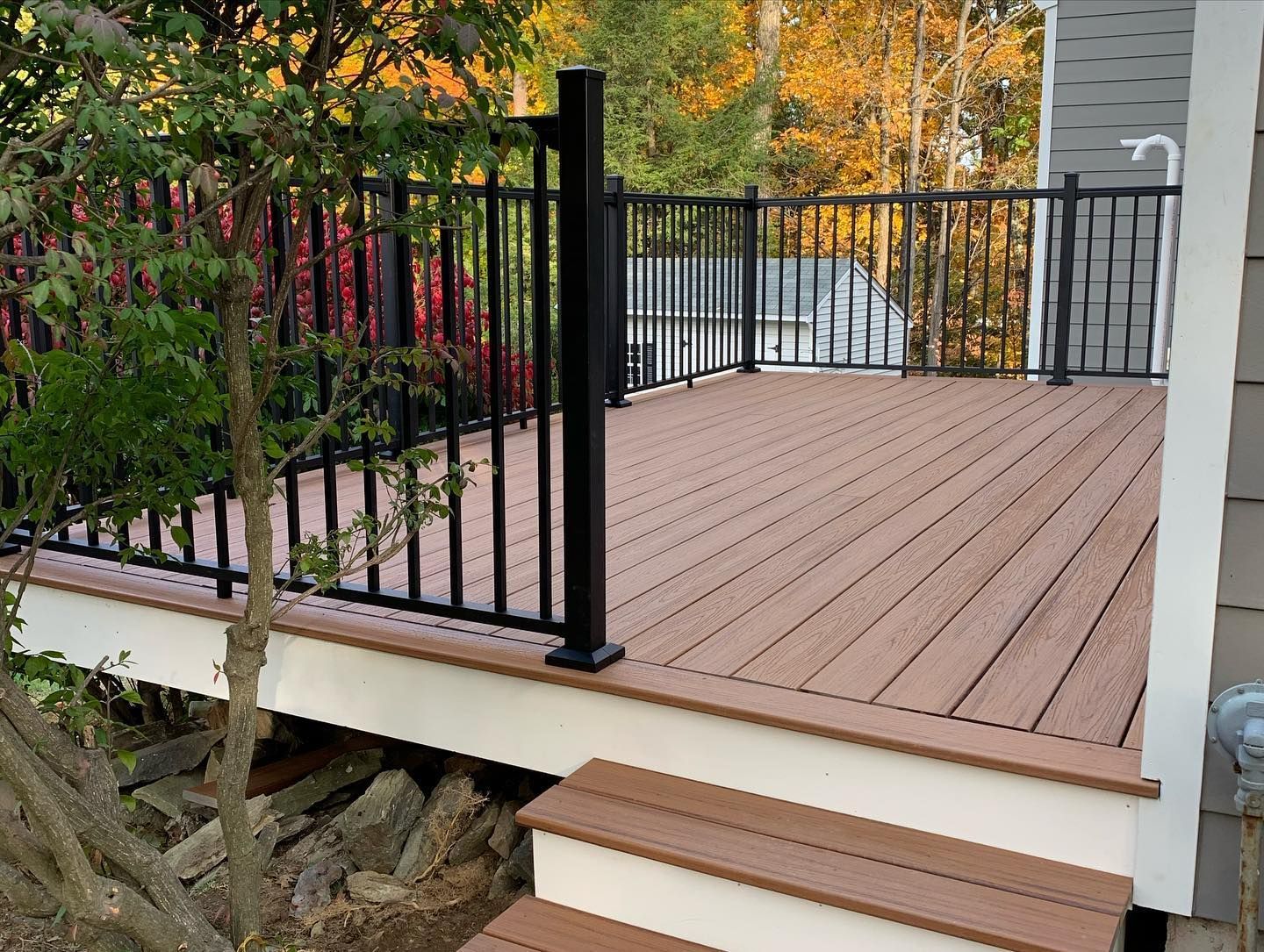 A raised wooden deck with black metal railings and stairs, positioned next to the side of a house.