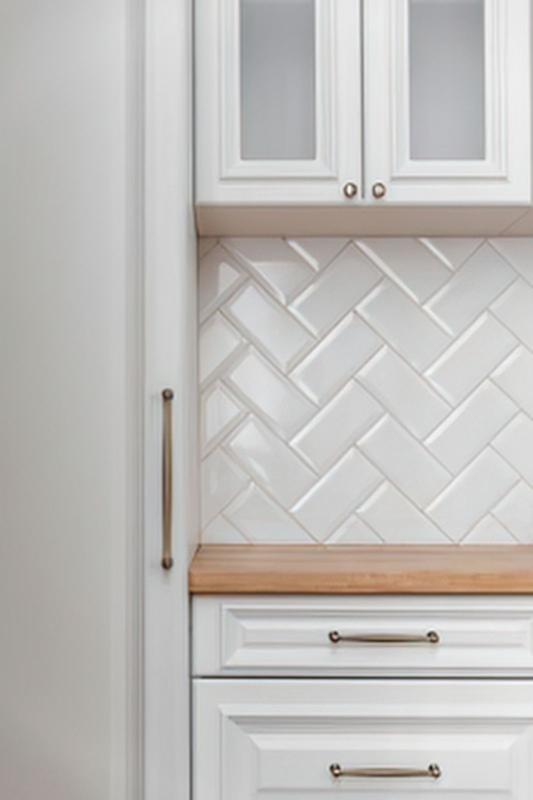 White kitchen cabinets with wood countertops and a herringbone patterned tile backsplash.