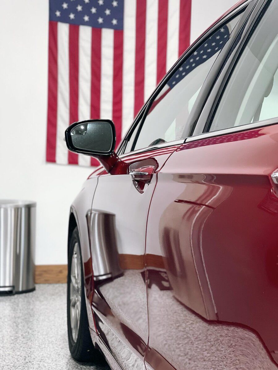 A red car is parked in front of an american flag