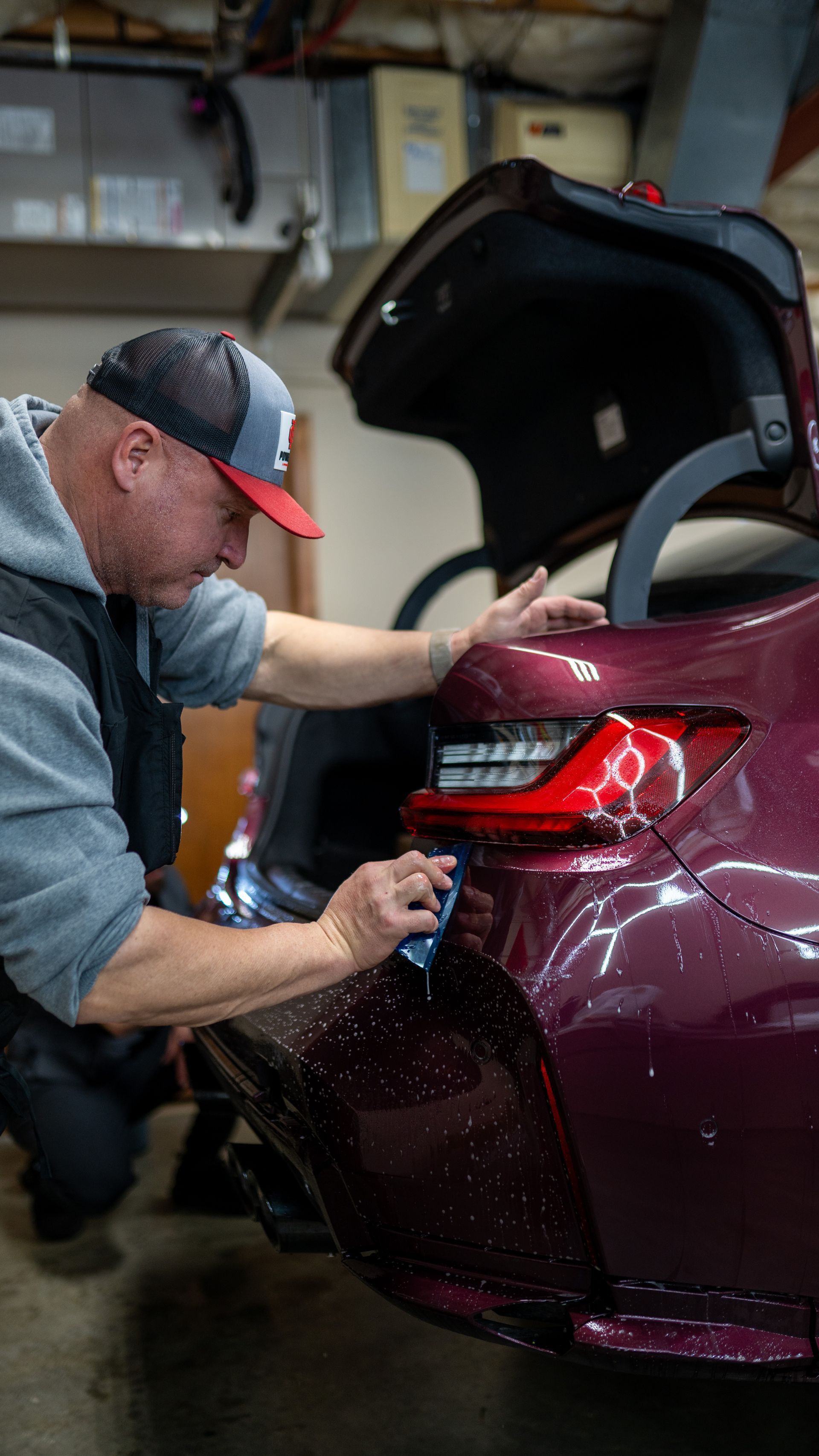 A man is applying a protective film to the back of a purple car.