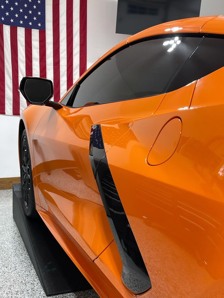 An orange sports car is parked in front of an american flag