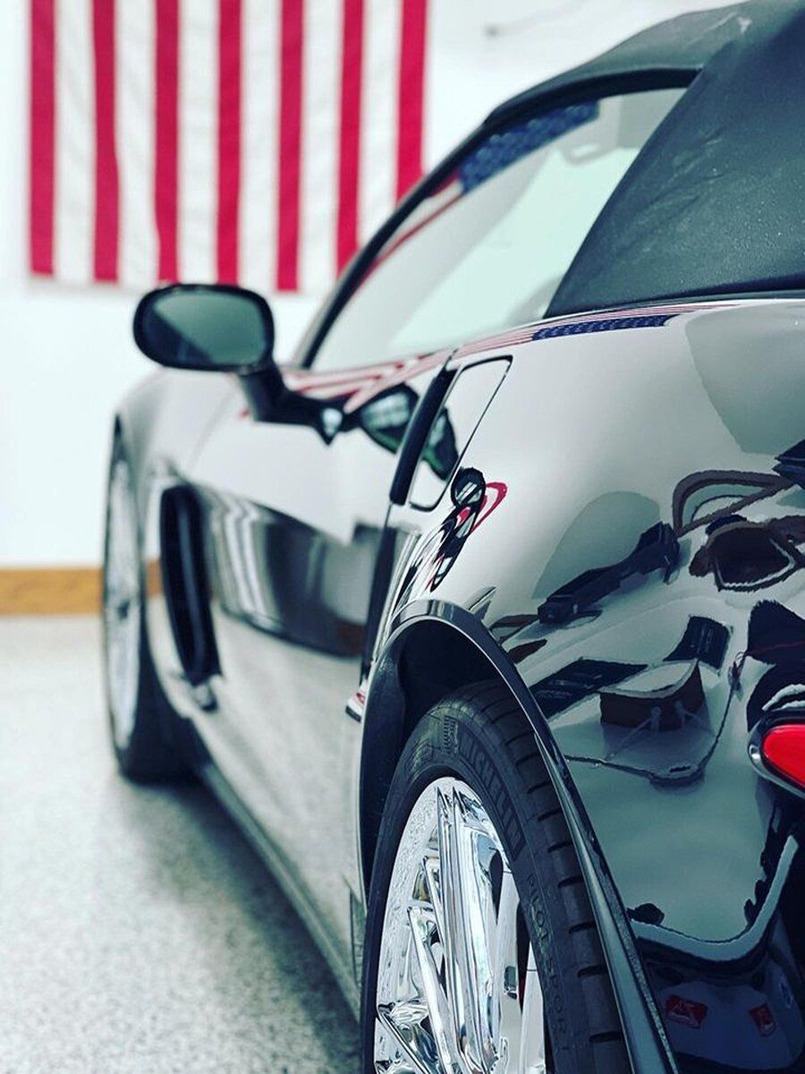 A black sports car is parked in front of an american flag