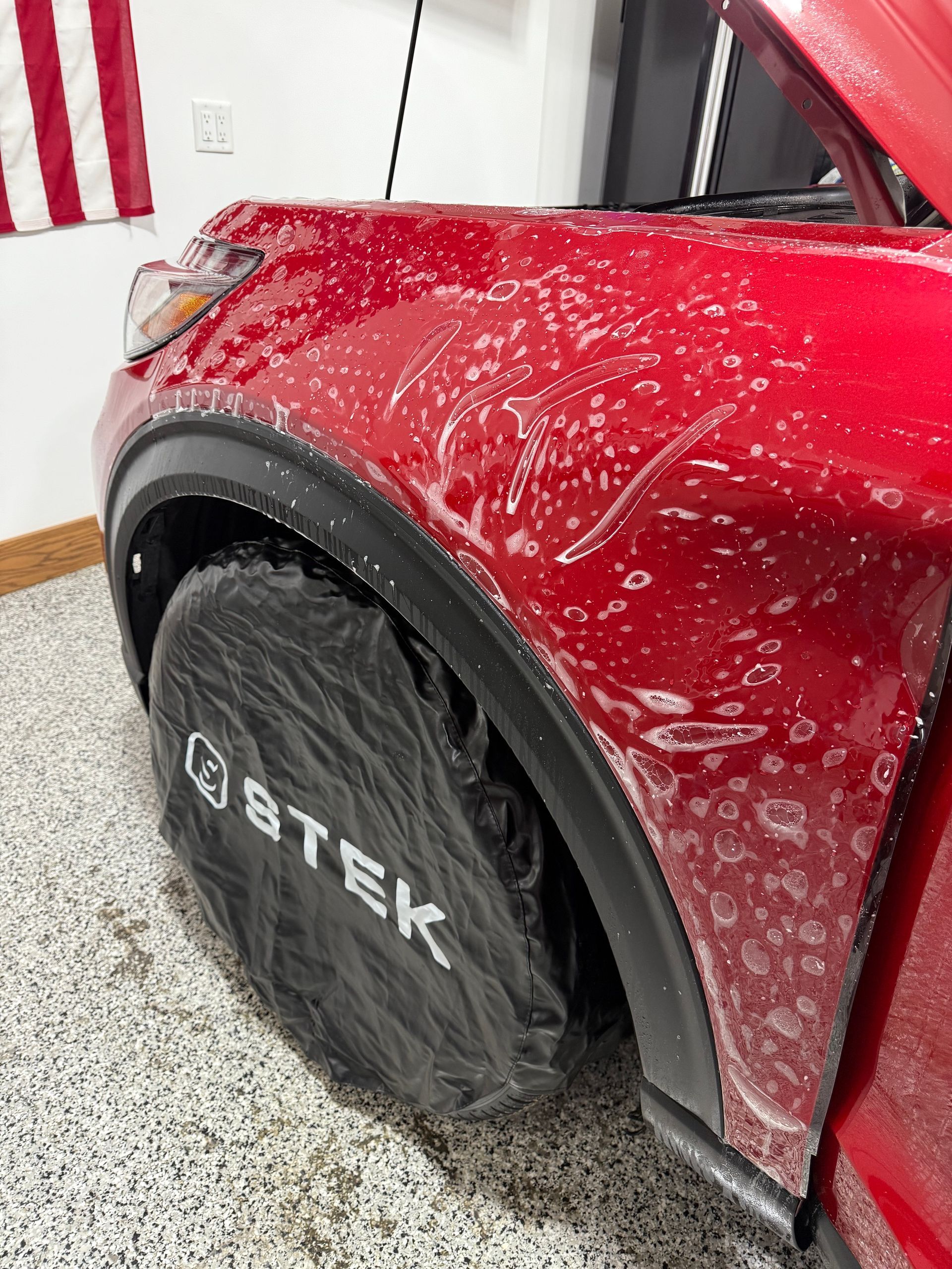 A red car is sitting in a garage with a tire cover on it.