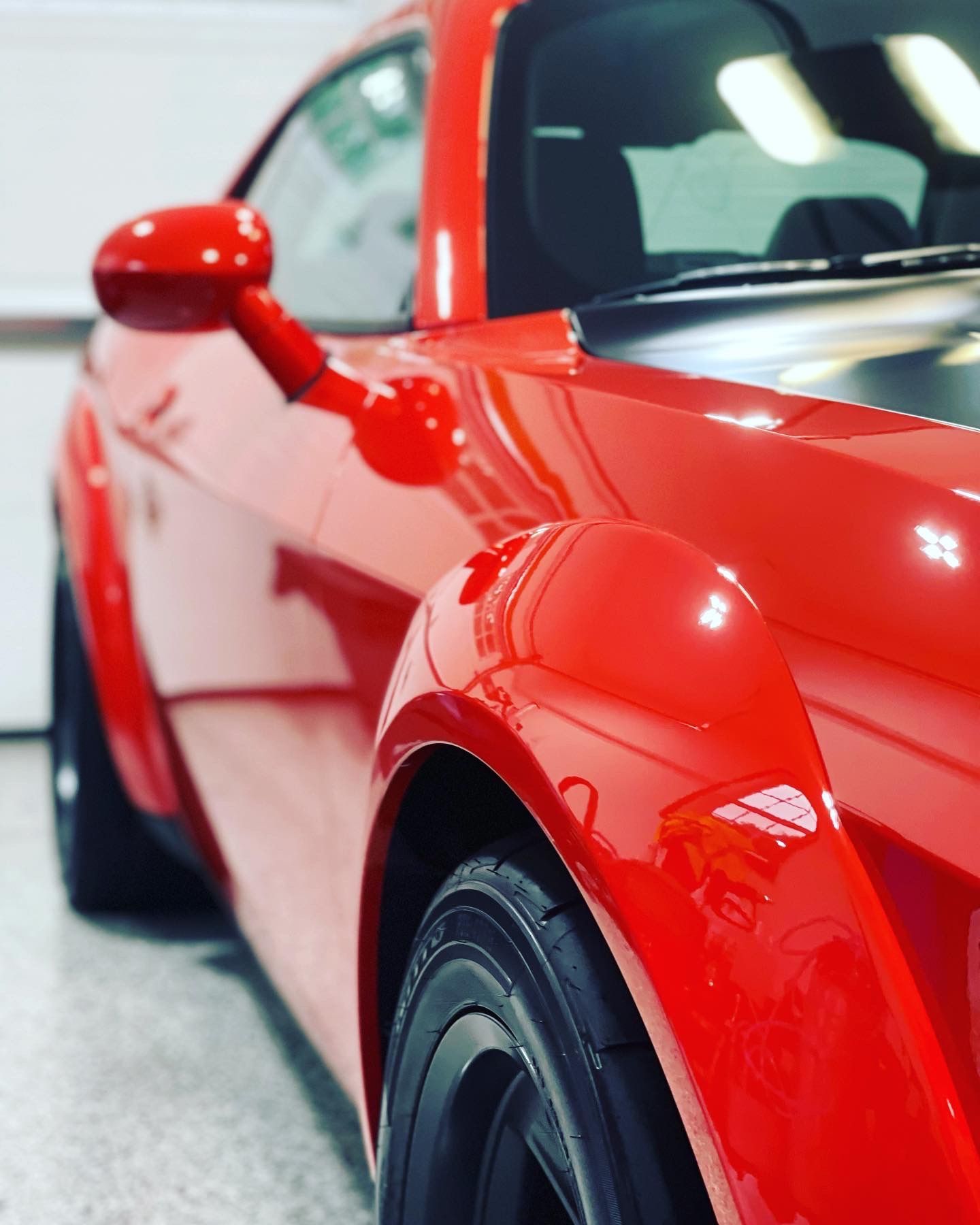 Bright red Dodge Challenger, close-up of side, front tire, and mirror, indoors with white background.