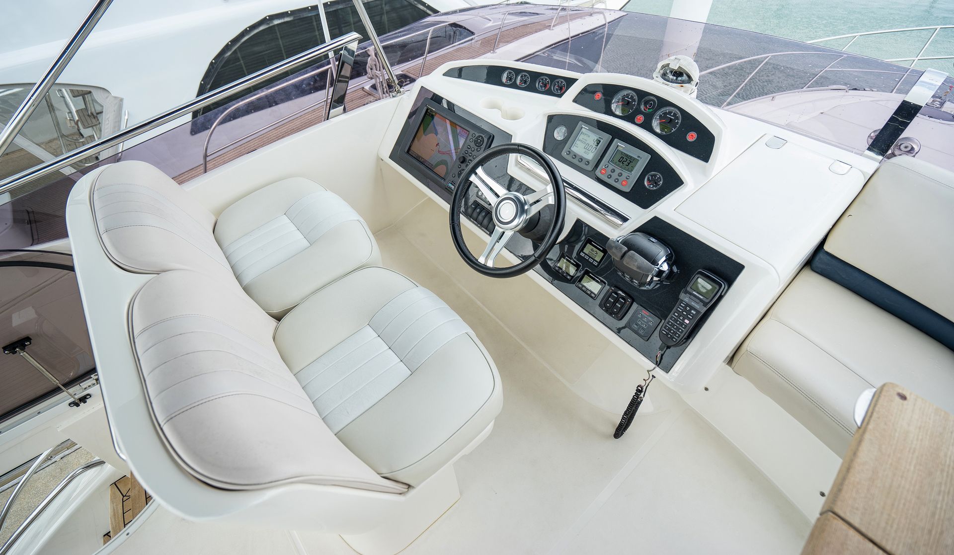 Boat helm with steering wheel, gauges, and white upholstered seats.