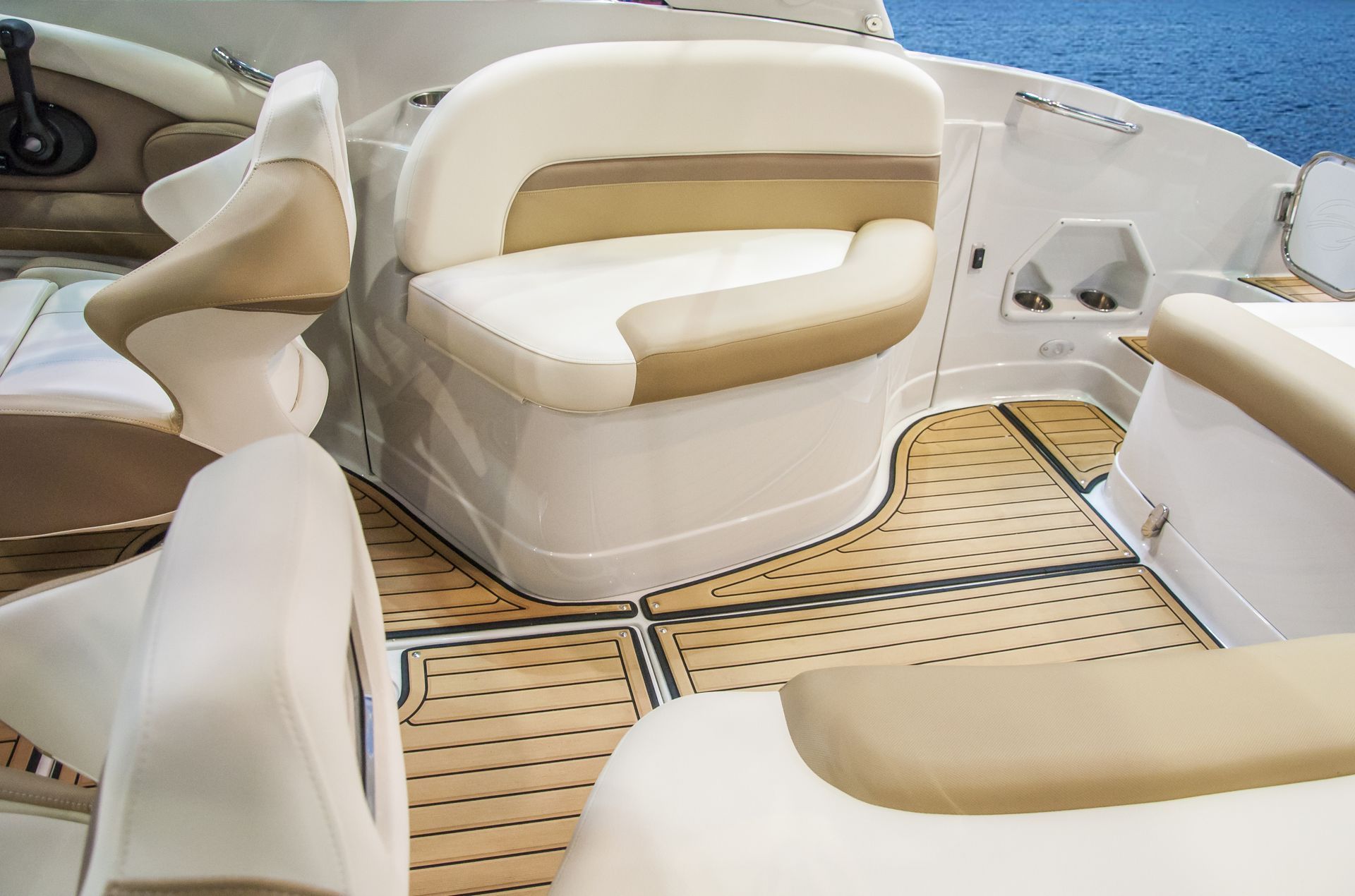 Boat interior with beige and white seating, wood-grain flooring, and blue water in the background.
