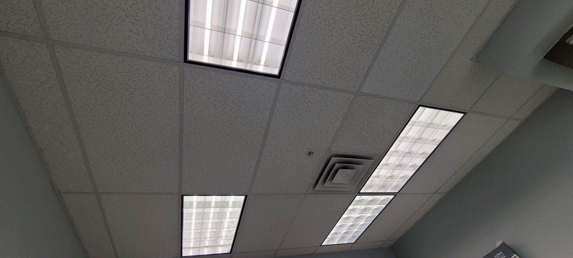 A ceiling with fluorescent lights and a vent in an office.