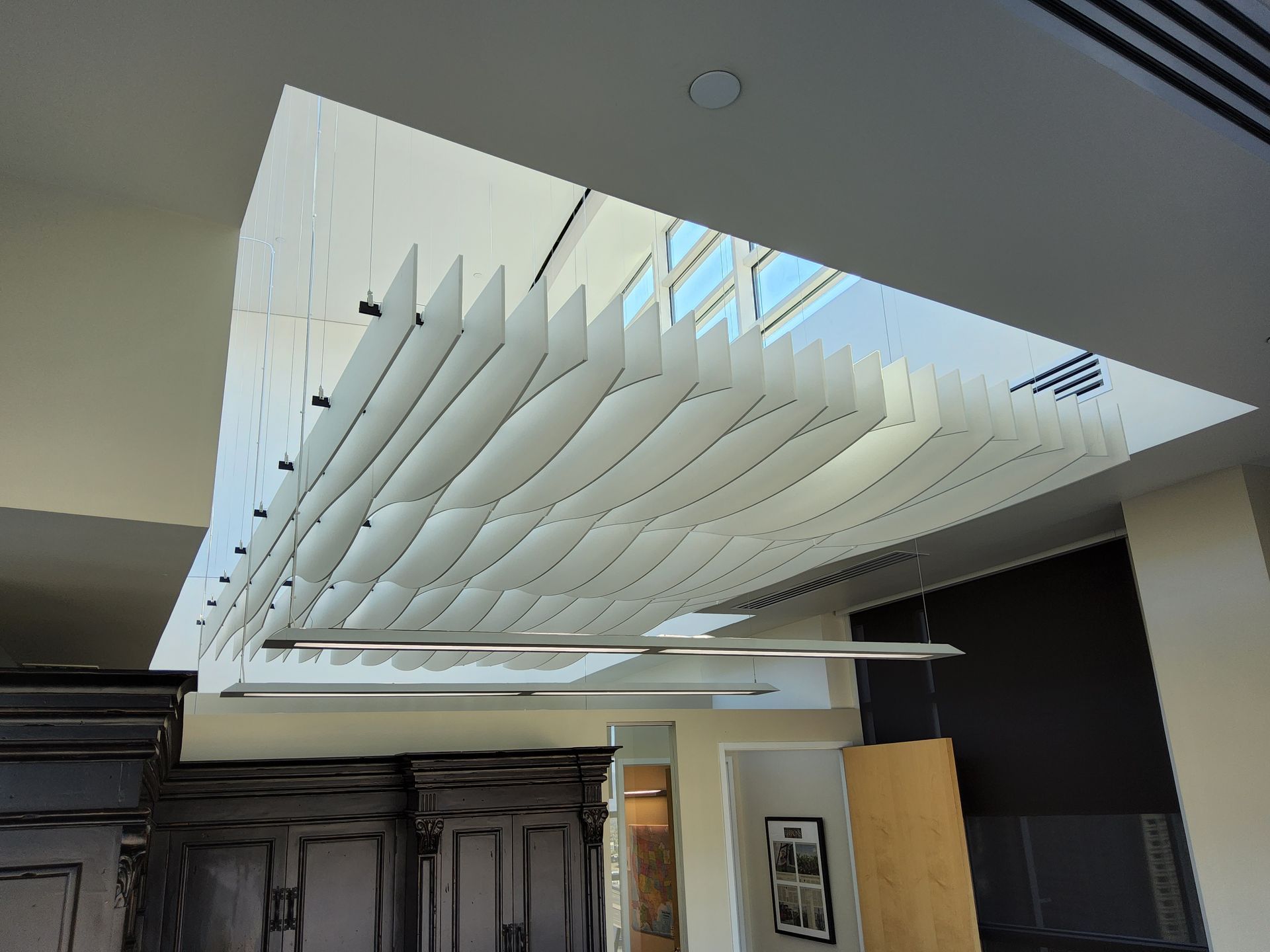 White, layered ceiling design above an interior with a light fixture and a glimpse of the outside.