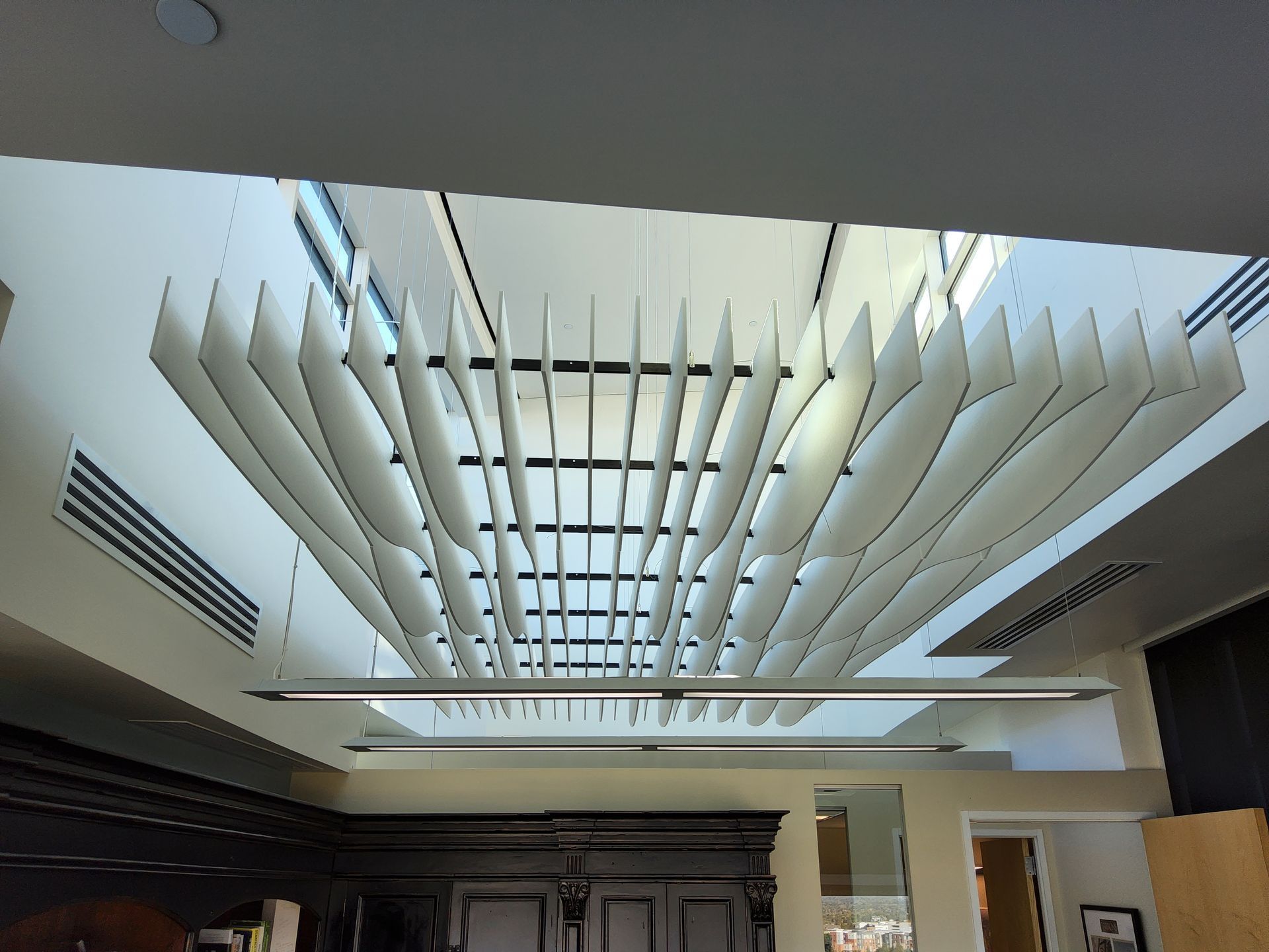 White, layered acoustic panels suspended from a high ceiling, with a skylight above.