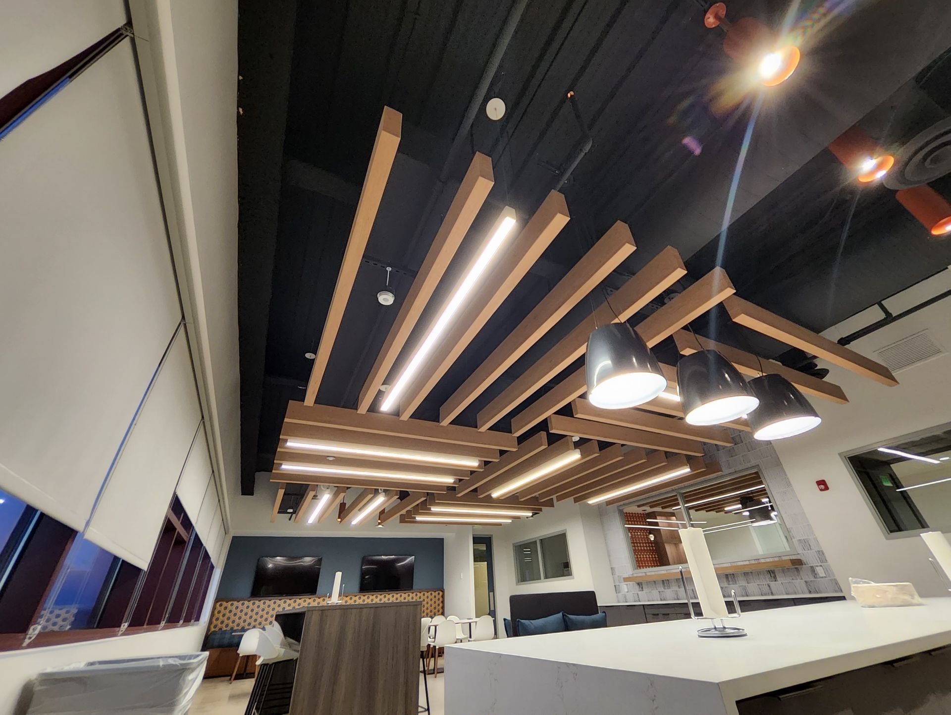 Modern office ceiling with geometric wooden beams, recessed lighting, and pendant lights.