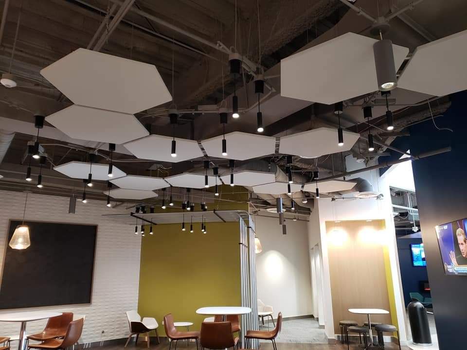 Modern cafe interior: white hexagon ceiling panels with spotlights, tables, chairs, and colorful walls.