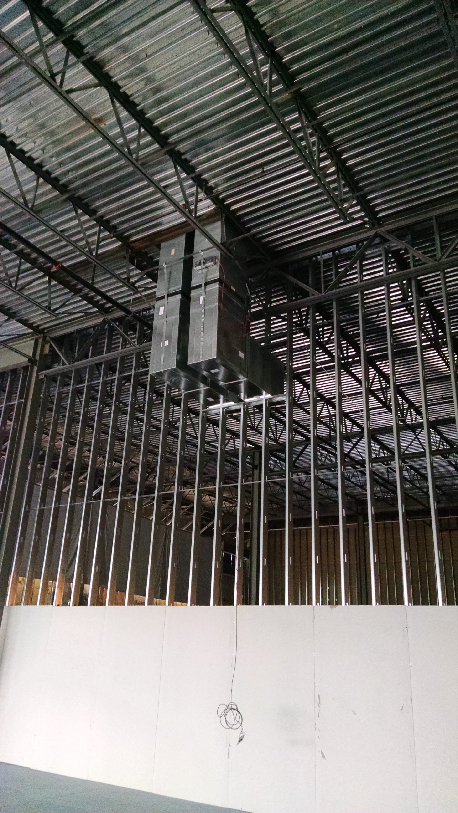 Metal framework of a building under construction, with speakers suspended from the ceiling.