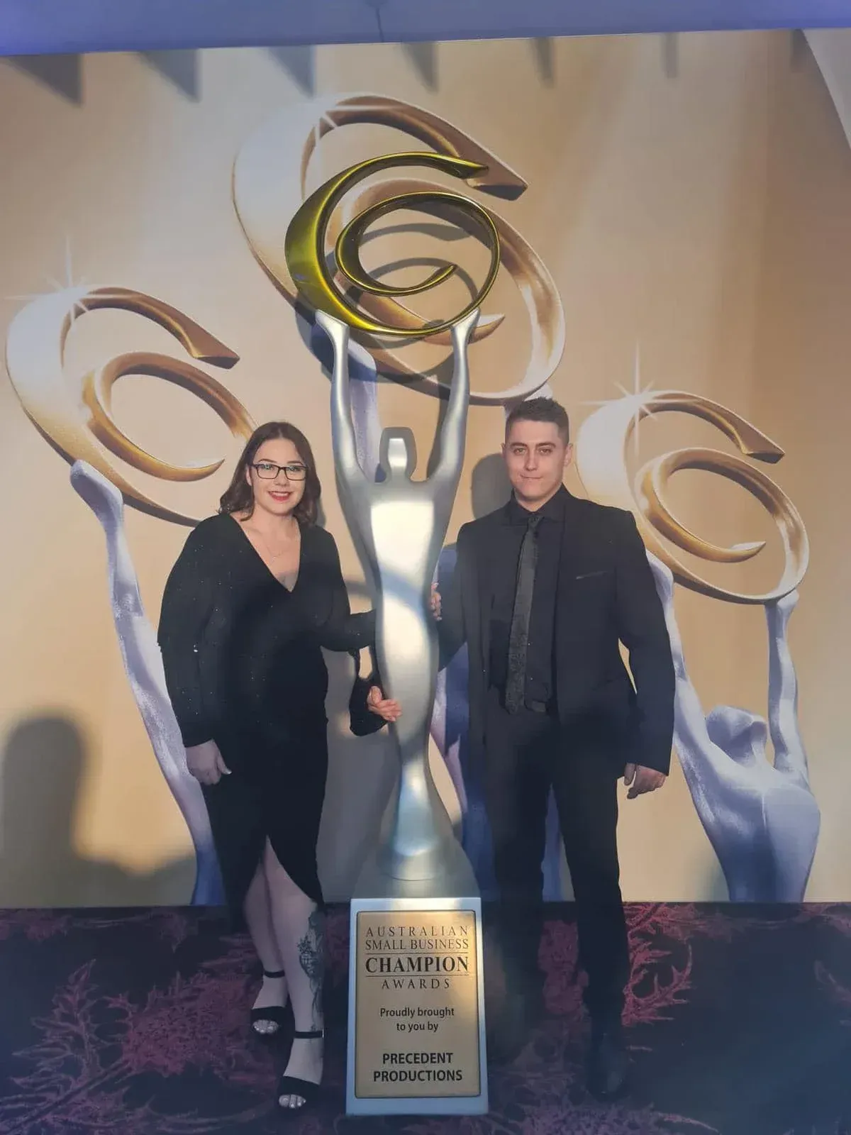 A man and a woman are standing next to a trophy.