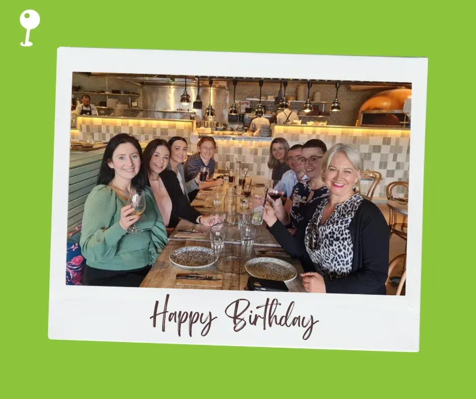 A group of people are sitting at a table holding glasses of wine.