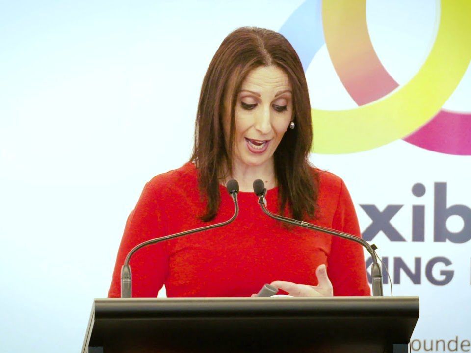 A woman is giving a speech at a podium in front of a sign that says xib