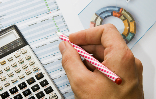 A person is writing on a piece of paper with a calculator in the background