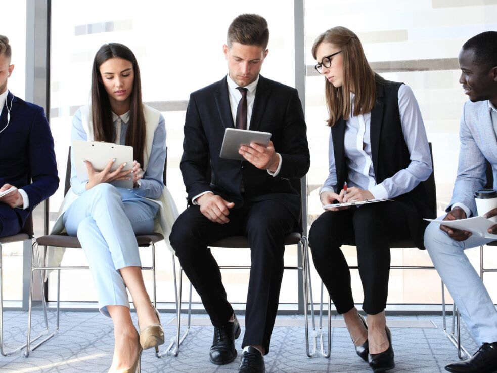 A group of people are sitting in chairs waiting for a job interview.