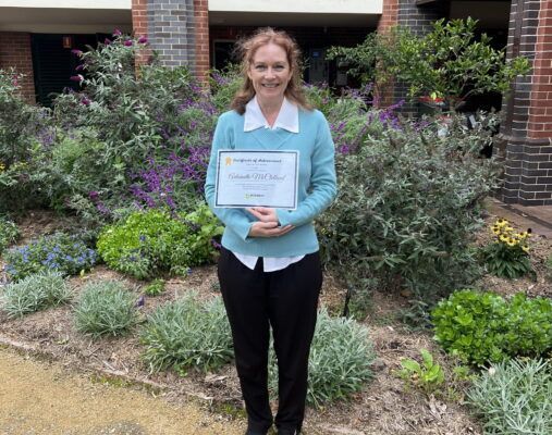A woman is standing in a garden holding a certificate.