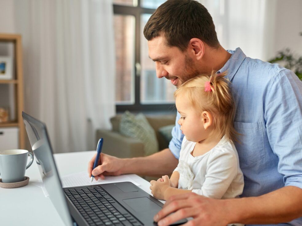 A man is holding a little girl while using a laptop computer.