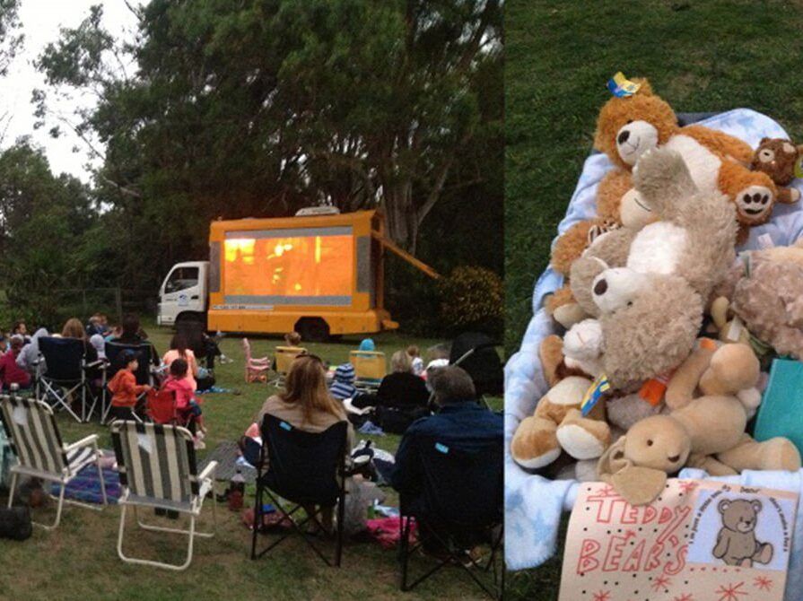 A bunch of stuffed animals are sitting on a blanket in front of a movie screen