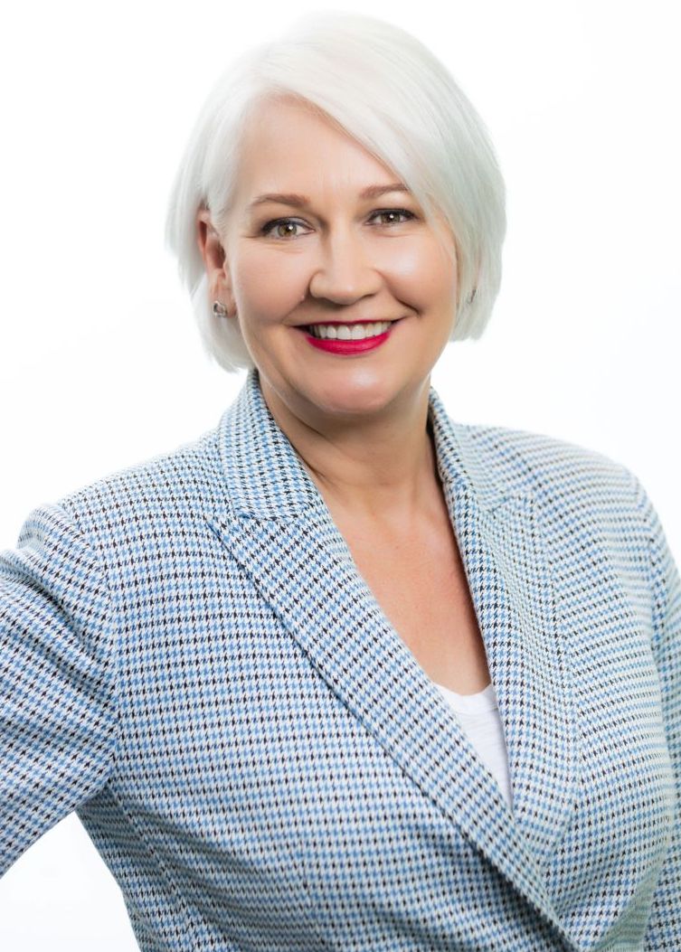 A woman with white hair is wearing a blue jacket and smiling.