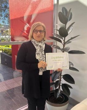 A woman is holding a certificate in front of a potted plant.