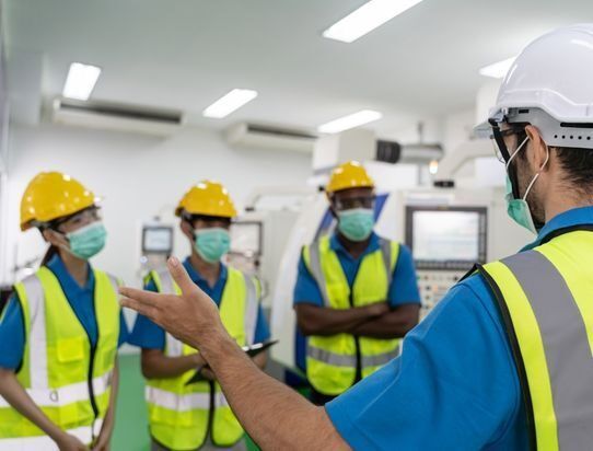 A group of construction workers wearing masks and hard hats are standing in a room.