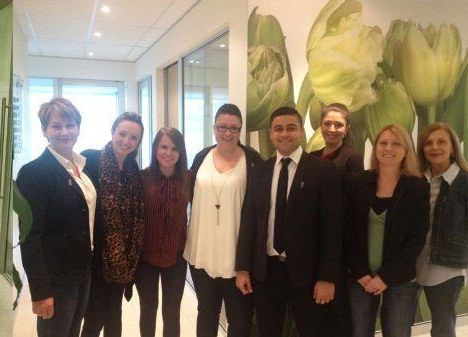 A group of people are posing for a picture in front of a wall with flowers on it.