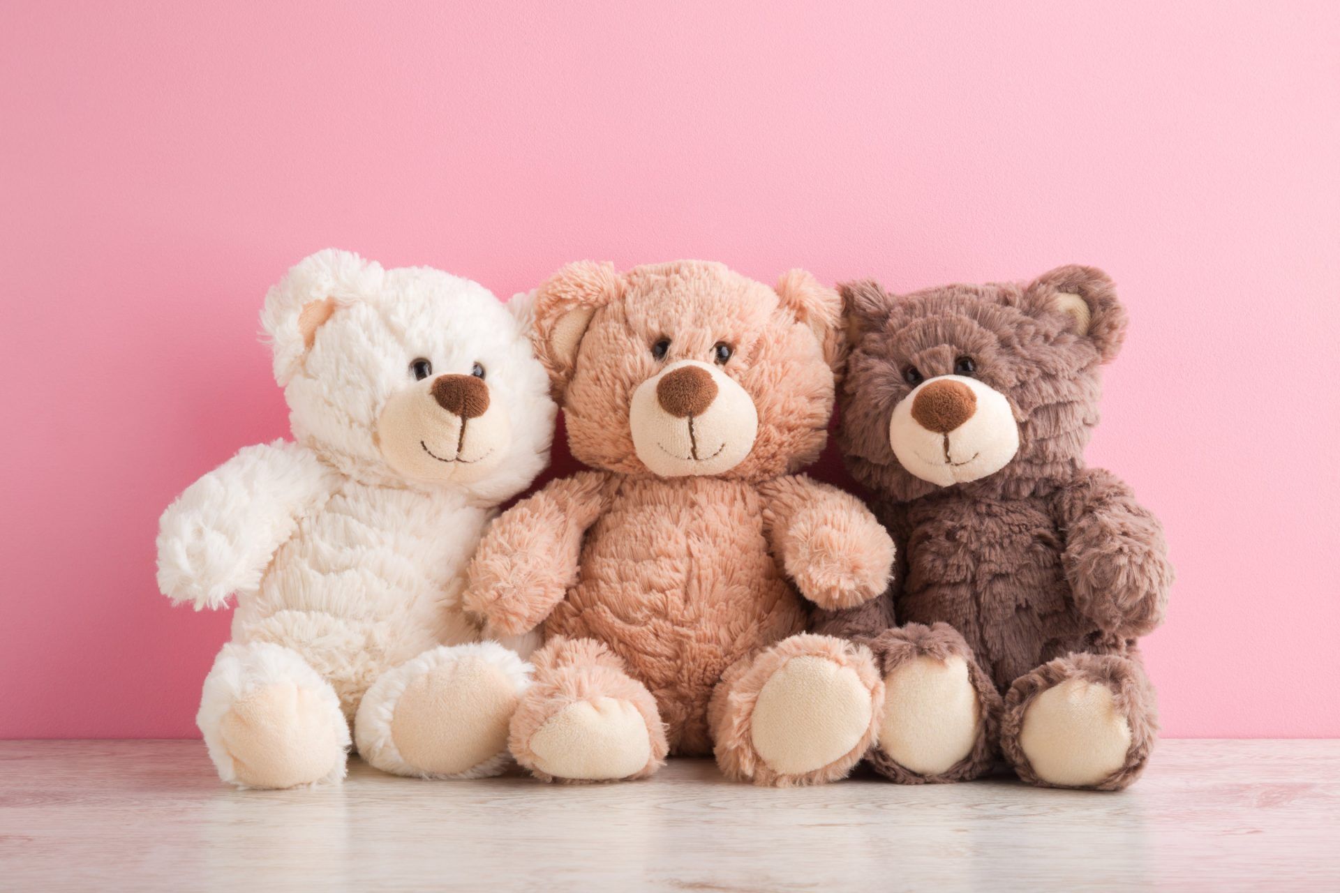 Three teddy bears are sitting next to each other on a pink background.