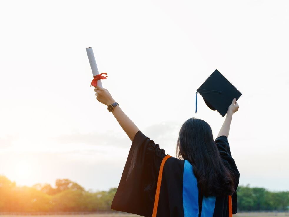 A woman in a graduation cap and gown is holding a diploma in her hand.