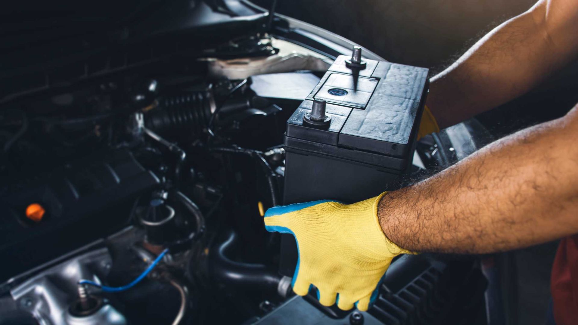 A man wearing yellow gloves is working on a car battery.