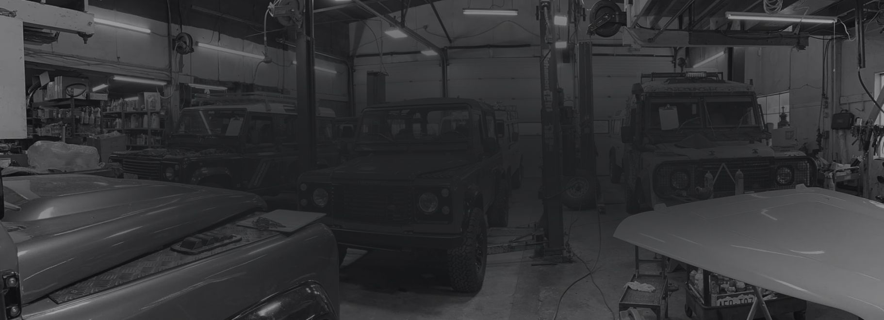 Interior of a dimly lit auto repair shop, a vehicle is center with work bays and tools visible.  | Artisan Autoworks