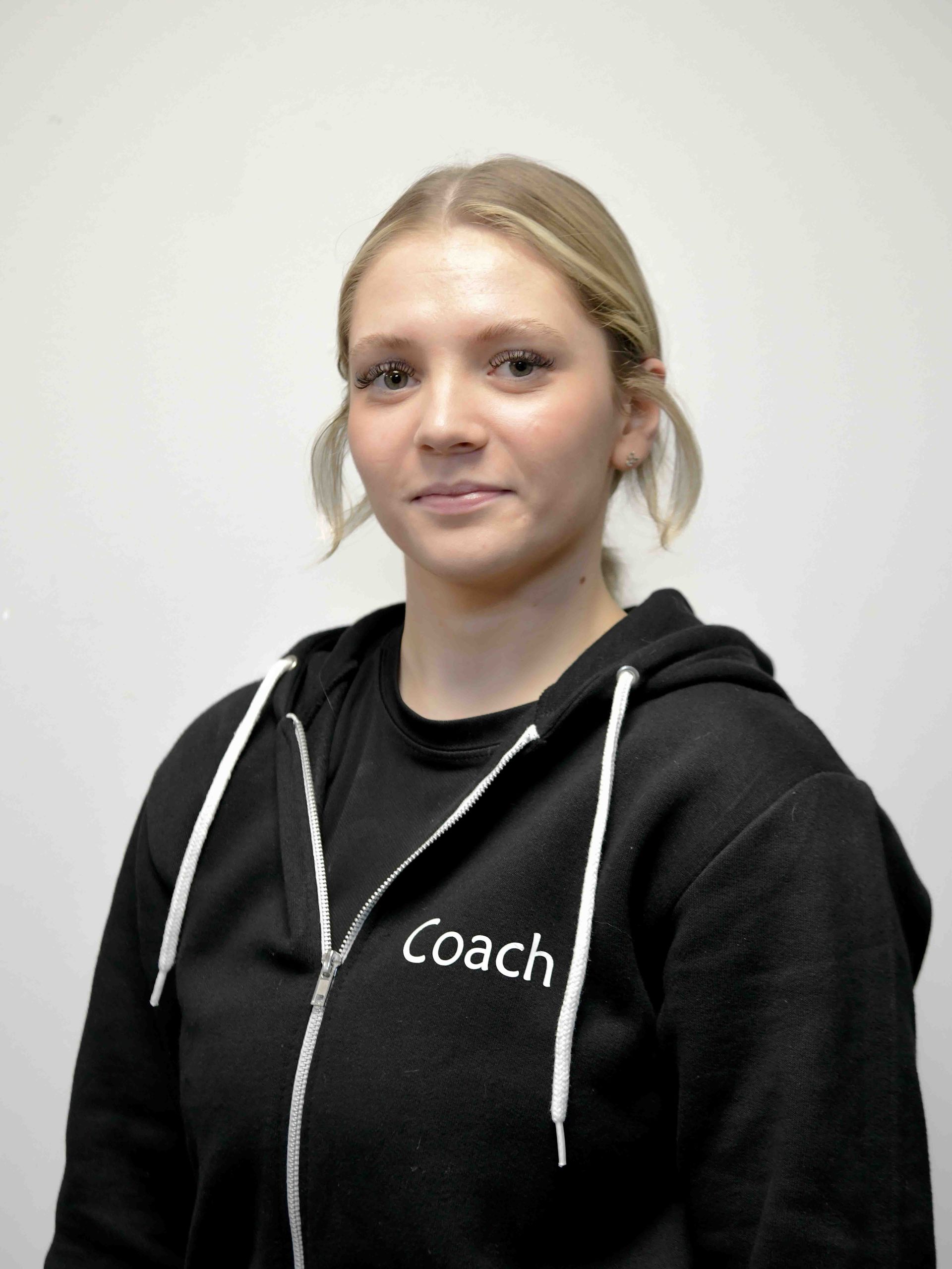 A woman wearing a black coach hoodie stands in front of a white wall