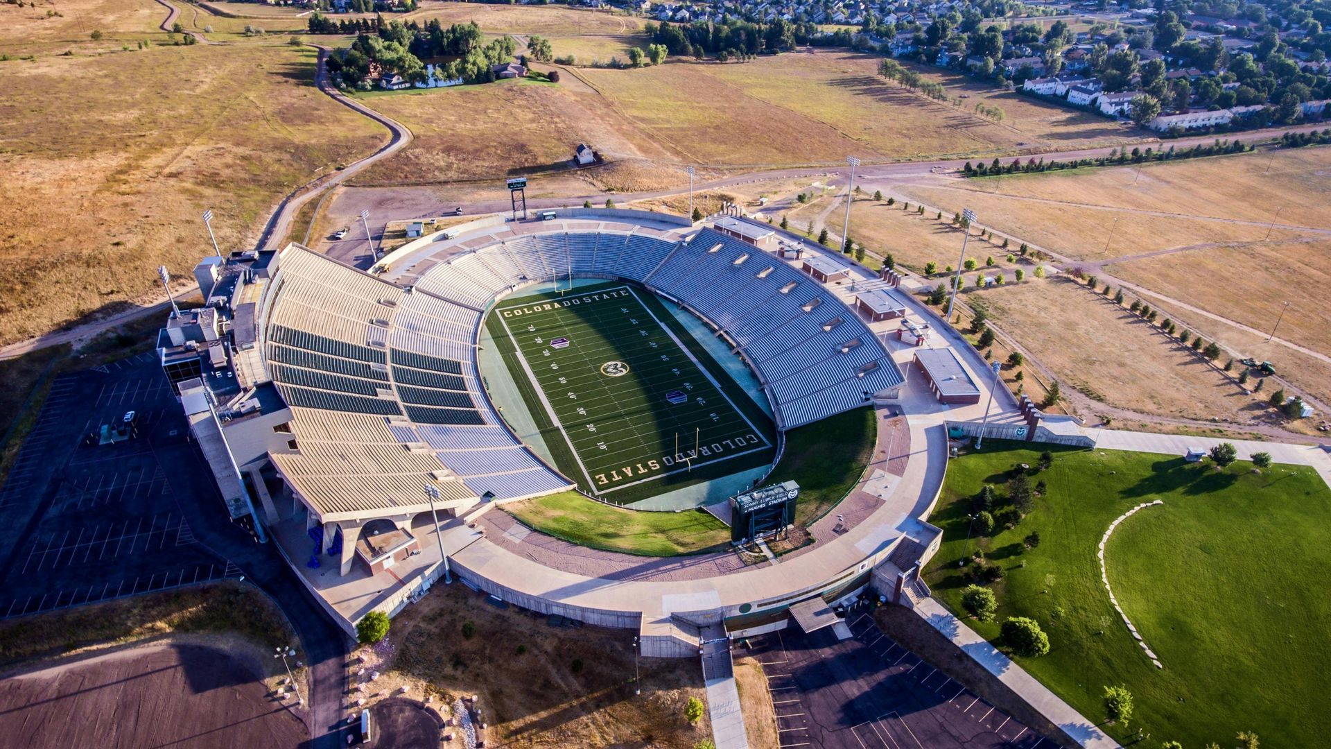 Aerial view of football stadium with green field, beige seating, and surrounding landscape.