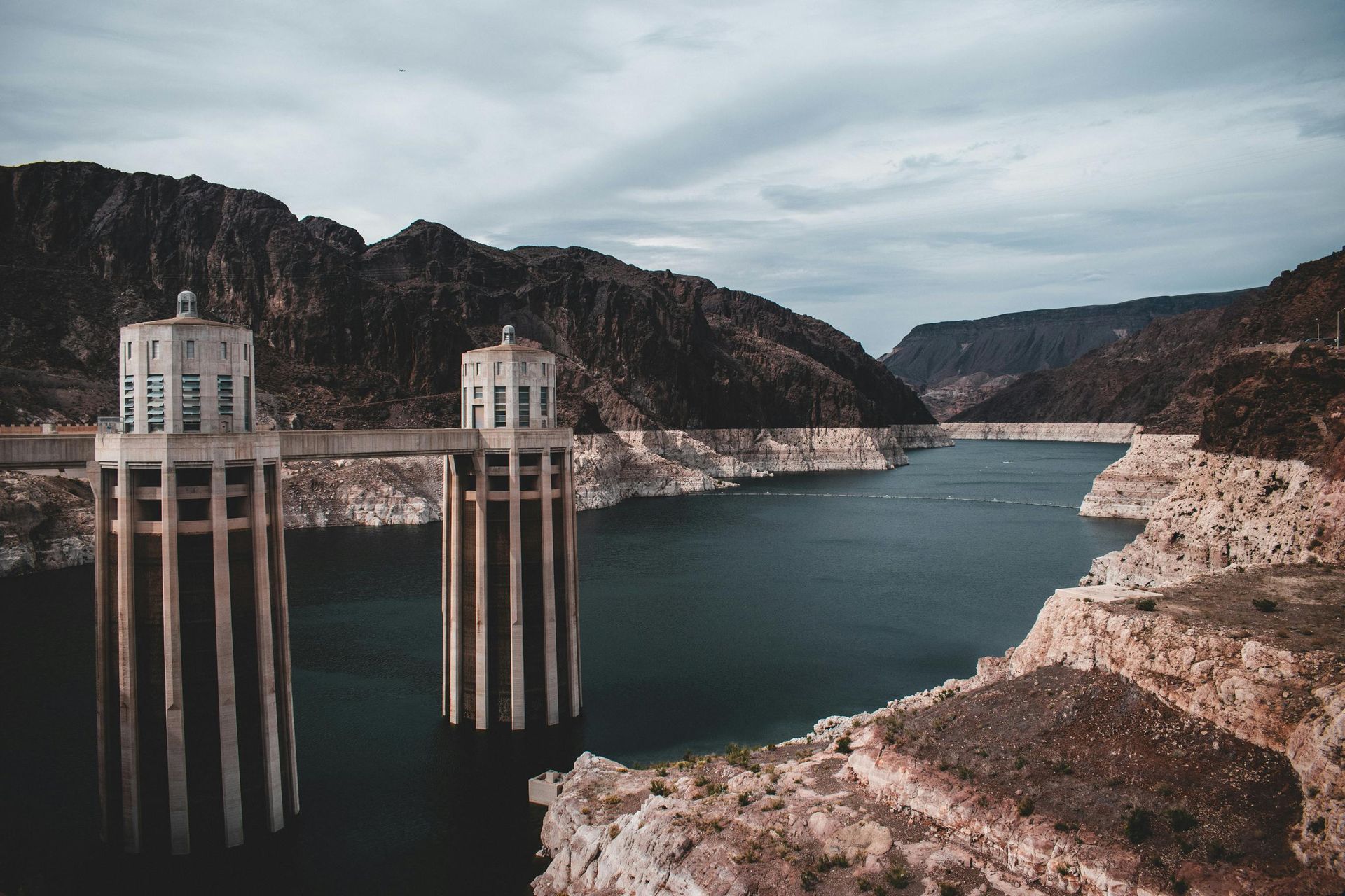 Dam with two tall towers, water reservoir, and canyon mountains.