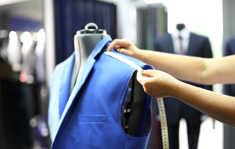 A woman is measuring a blue suit jacket on a mannequin.