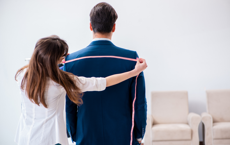 A woman is measuring a man 's shoulder with a tape measure.