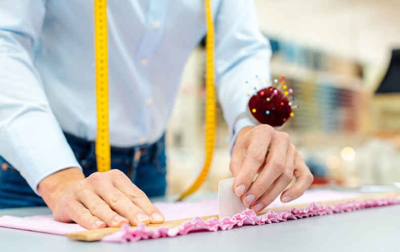 A man is measuring a piece of fabric with a tape measure.